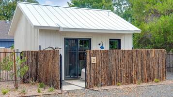 A small, single-story building with a white exterior and a sloped metal roof. There is a wooden fence in front, and a small number '2' sign on the fence.