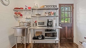 A compact kitchen with stainless steel appliances, a clock, and a 'CHEERS' sign. - Ava and Weston Combo House (Fredericksburg)