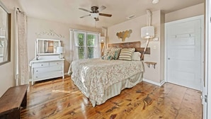 A bedroom with a bed, a dresser, a ceiling fan, a window, and a door. - Ava and Weston Combo House (Fredericksburg)