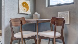 Quarto com duas cadeiras de madeira, uma mesa pequena, toalha pendurada com o símbolo yin-yang e uma obra de arte emoldurada na parede.