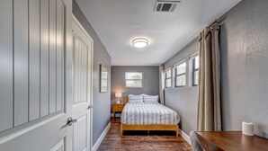 Quarto com cama de madeira, mesa de cabeceira, luminária e janela com cortinas.