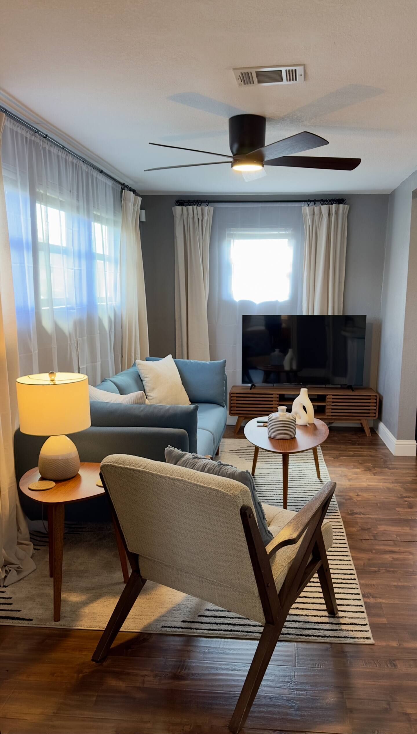 Ein modernes Wohnzimmer mit einer Couch, einem Sessel, einem Fernseher und einem Deckenventilator.