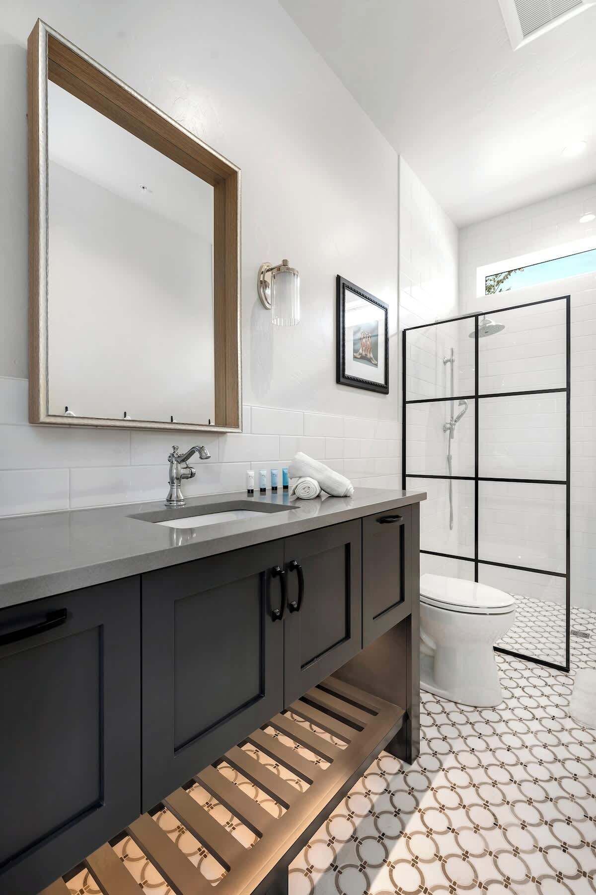 Un baño moderno con un espejo grande, un lavamanos con grifo, un cuadro enmarcado y una zona de ducha con puerta de cristal.