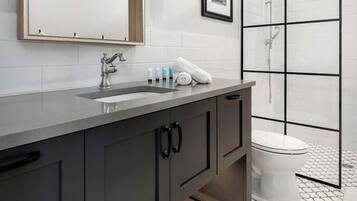 Un baño moderno con un espejo grande, un lavamanos con grifo, un cuadro enmarcado y una zona de ducha con puerta de cristal.