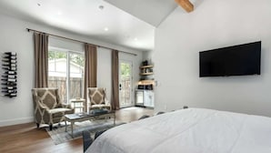 Een ruime slaapkamer met een groot bed, een flatscreen televisie aan de wand en een schuifdeur naar een balkon.