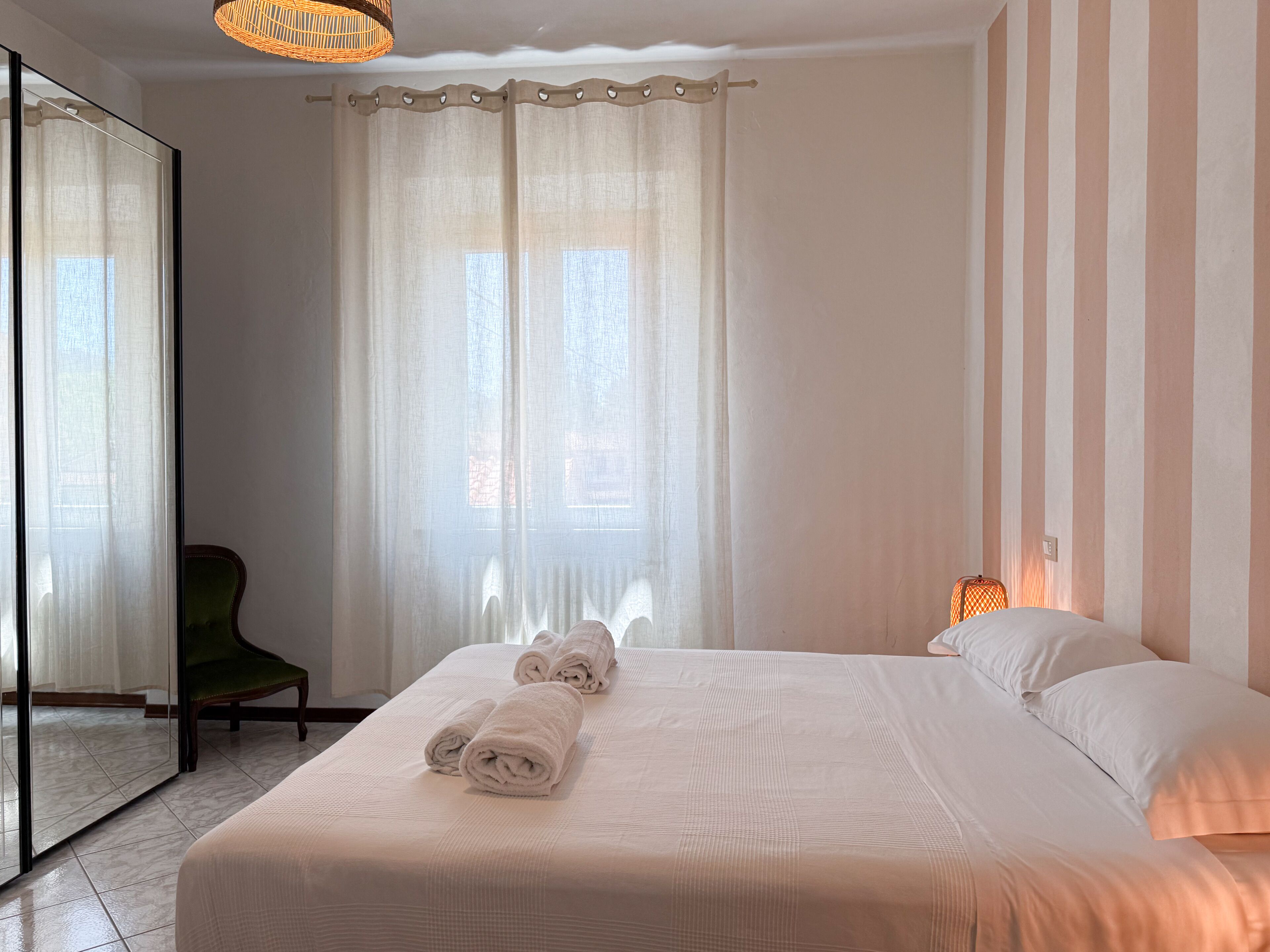Un dormitorio con una cama grande, una silla, un espejo y una ventana con cortinas.