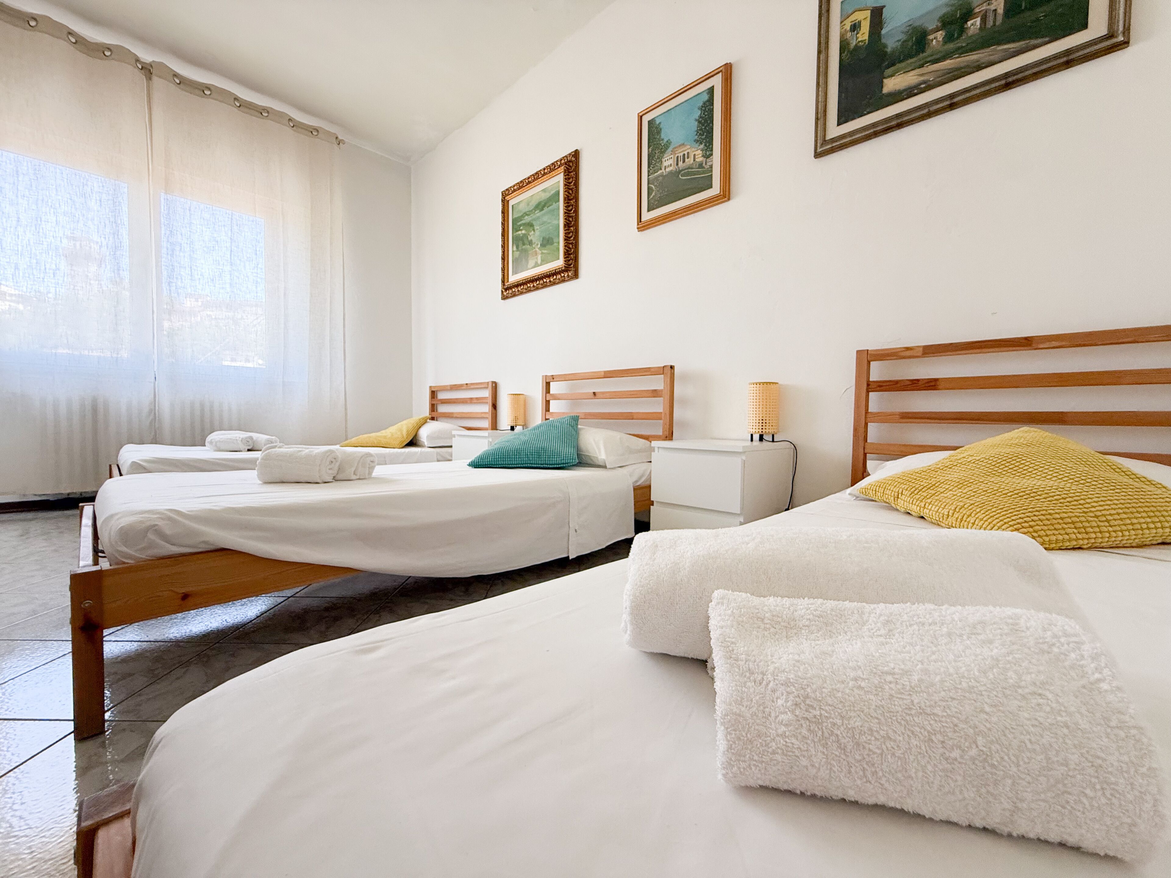 A hotel room with two beds, a nightstand, a lamp, and two framed pictures on the wall.