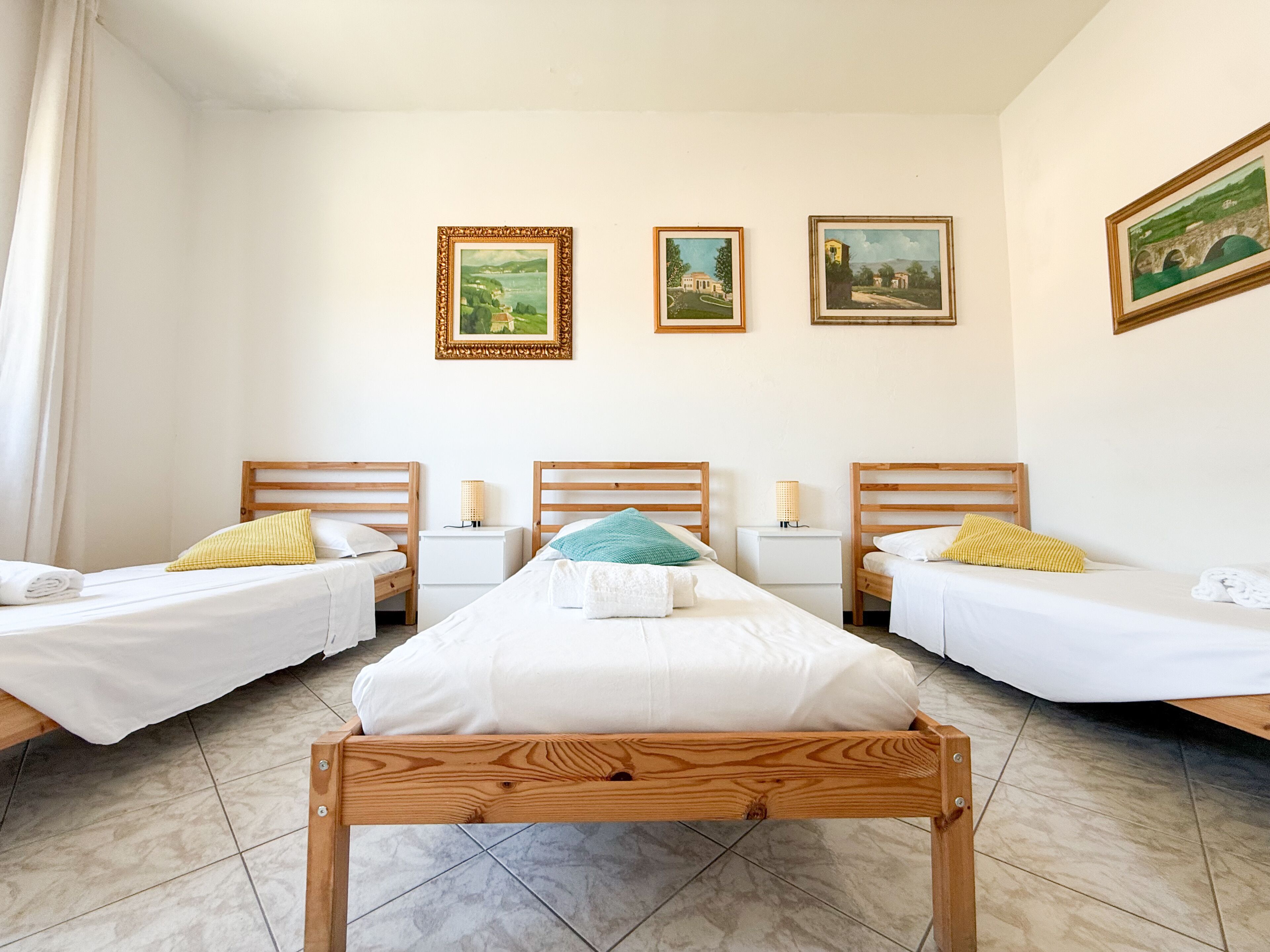 Quarto de hotel com duas camas de solteiro, uma cama maior e três quadros na parede.