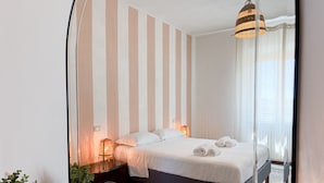 Ett modernt hotellrum med en säng, sänglampor, en krukväxt och en stor spegel.