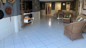A spacious living area with a tiled floor, wicker furniture, and a flat-screen TV mounted on the wall.