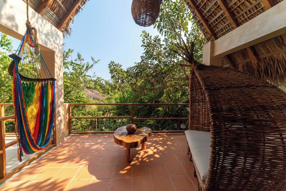A balcony with a wicker chair, a hammock, and a wooden table with a decorative bowl.