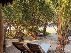 Un área de descanso frente al mar con sillones de madera, una estructura de techo de paja y palmeras.