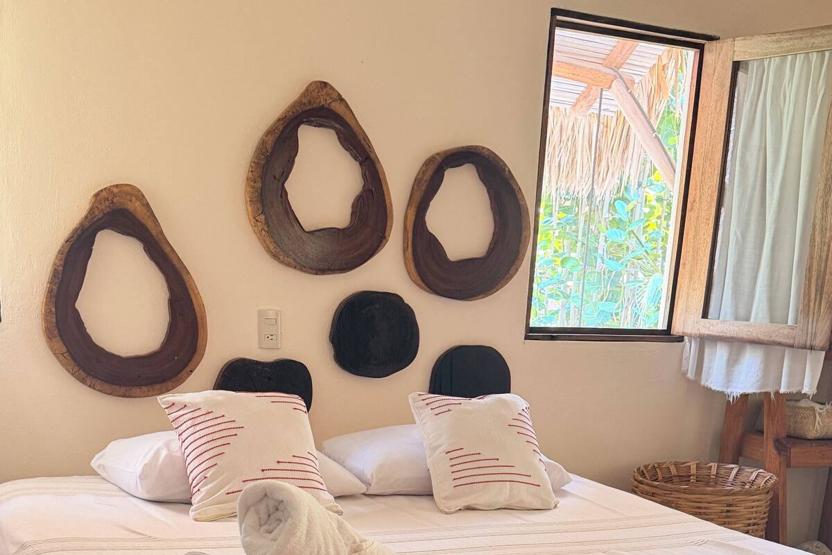A neatly made bed with white linens, a rolled towel, and decorative wooden rings on the wall.