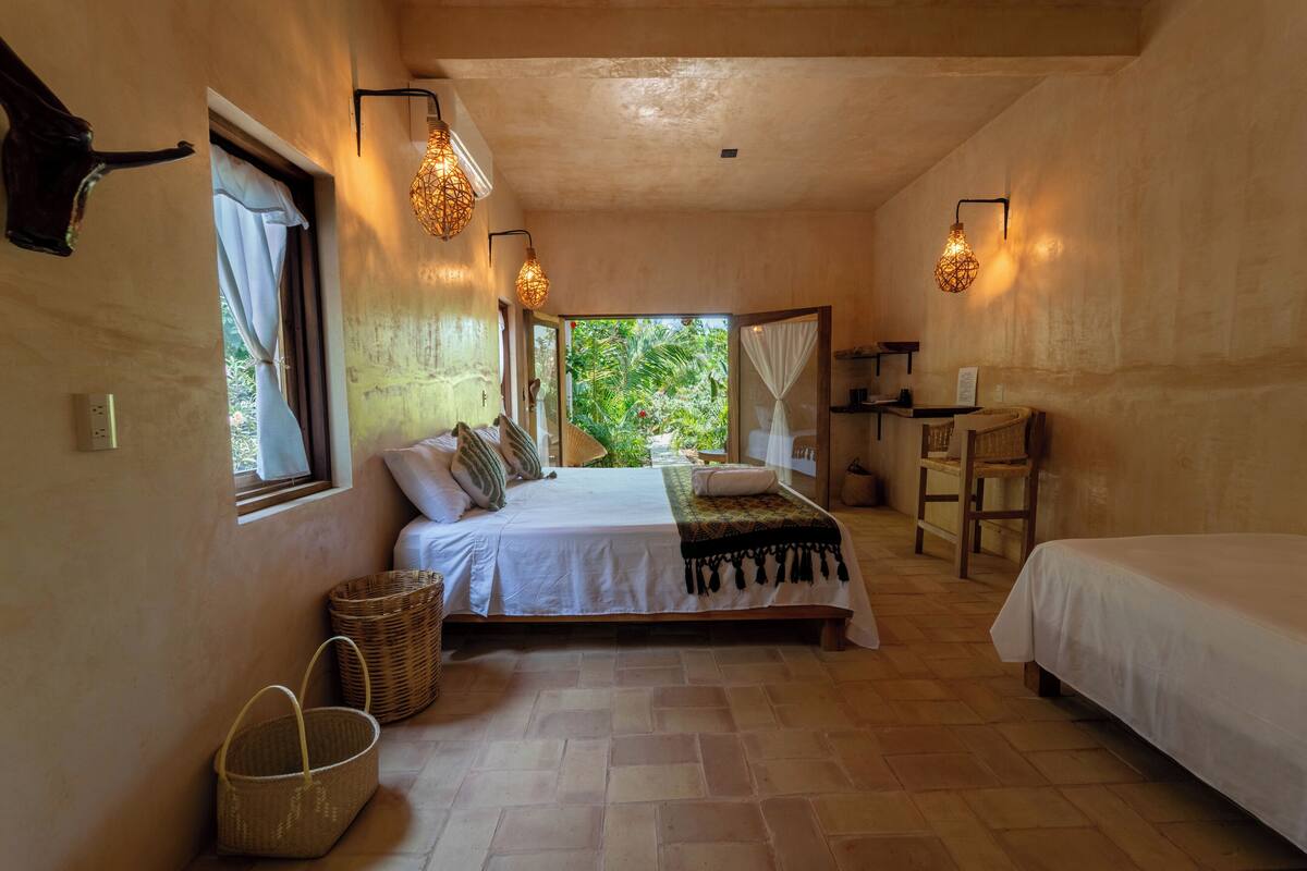 A bedroom with a large bed, two bedside tables, a window with curtains, and a view of greenery outside.