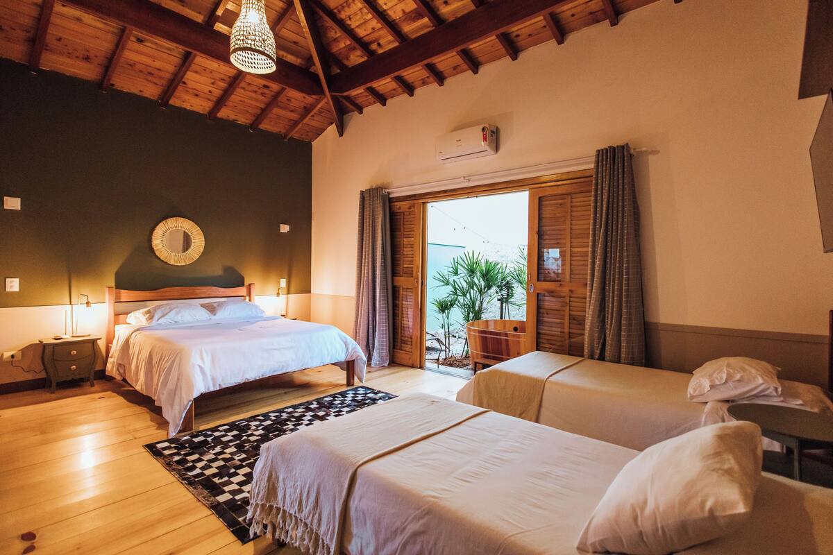 Een kamer met twee bedden, een houten plafond, een groot raam met gordijnen en een kleine tafel met een stoel.