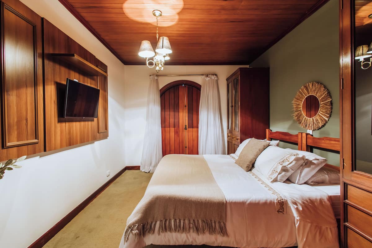 Een slaapkamer met een houten plafond, een bed met wit beddengoed, een tv aan de muur en een spiegel.