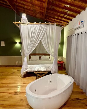 Quarto com cama de dossel, uma banheira grande e teto de madeira.