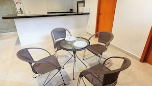 Een eetgedeelte met rieten stoelen en een ronde tafel, een keukenblad en een houten plafond.