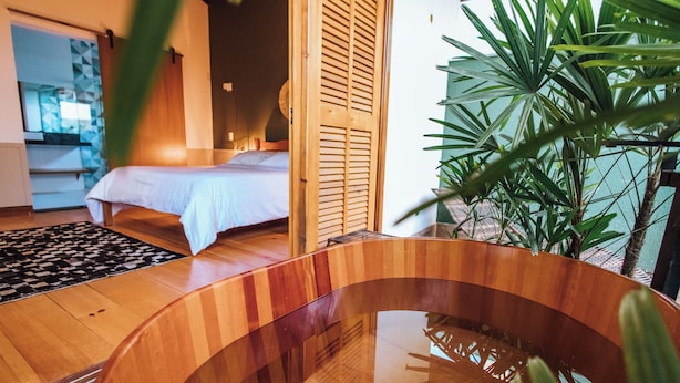 Een houten bad in een kamer met een bed en een grote plant.