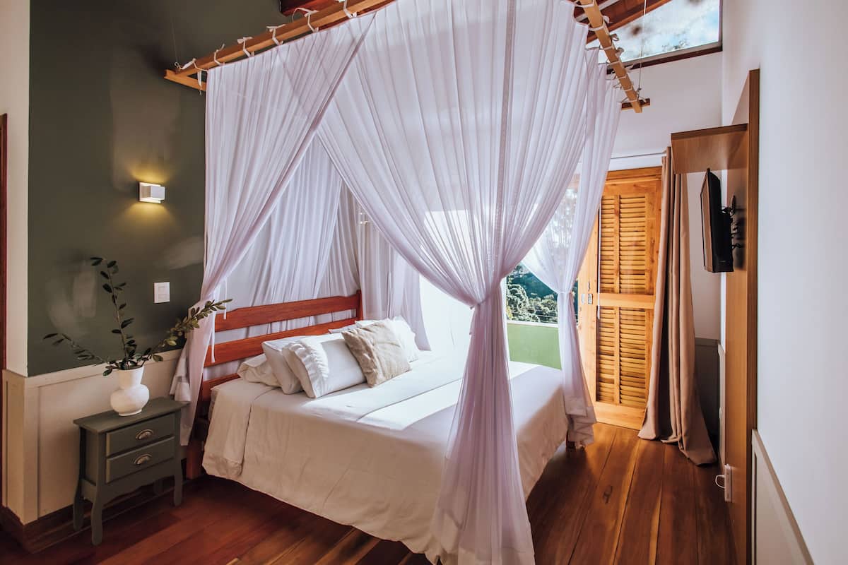 Een slaapkamer met hemelbed, nachtkastje en een bloempot.