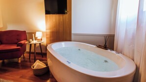 Een kamer met een groot bad, een rode stoel, een klein tafeltje met een lamp en een televisie aan de muur.