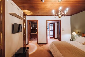 A hotel room with a wooden ceiling, a TV mounted on the wall, a bed with a beige comforter, a nightstand with a lamp, and a wardrobe. -  Smart Hotel Reserva Campos do Jordão (Campos do Jordão)