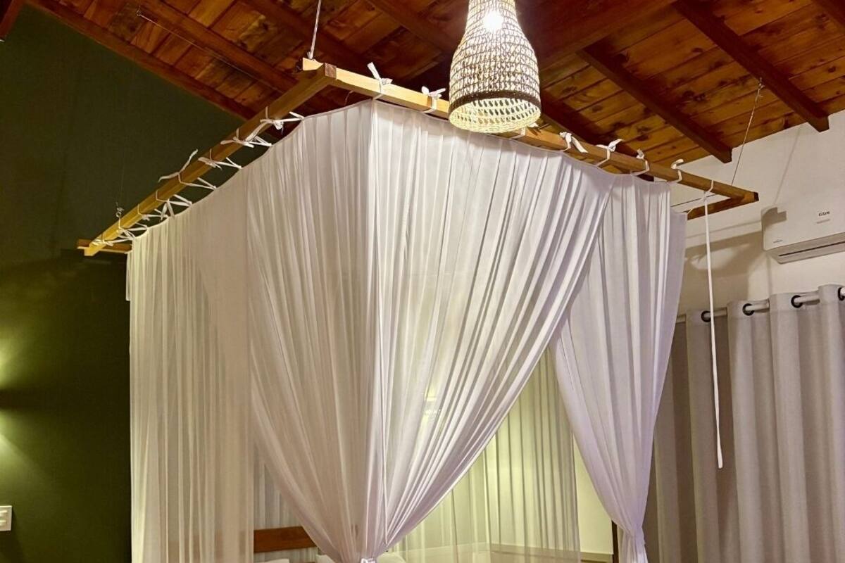 A room with a four-poster canopy bed, wooden flooring, and a chandelier.