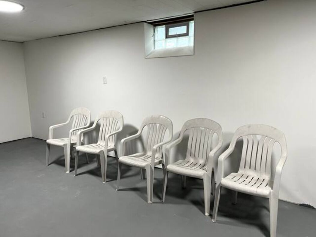 Cuatro sillas de plástico blanco dispuestas en fila frente a una pared lisa con un ventanal pequeño.