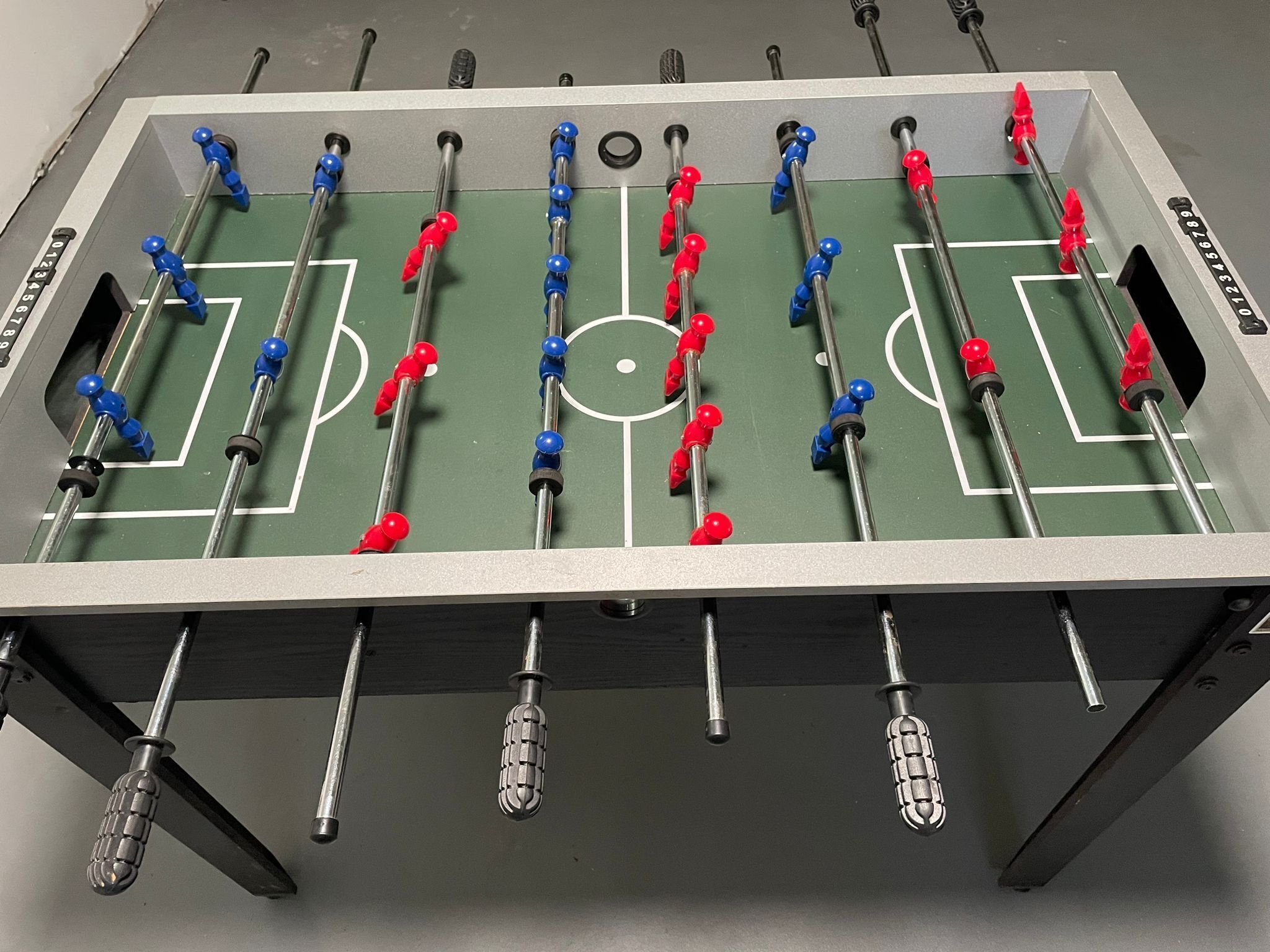 Ein Kicker mit einer grünen Spielfläche und Metallstangen mit roten und blauen Spielfiguren.
