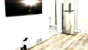 Ein Zimmer mit einem wandmontierten Flachbildfernseher, einem Edelstahlkühlschrank und Holzboden.