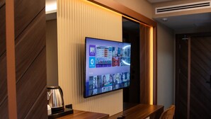 Une chambre d’hôtel avec un bureau en bois, un téléviseur à écran plat fixé au mur, une machine à café et une chaise.