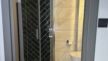 Un baño con ducha de mampara de vidrio, inodoro y lavamanos.