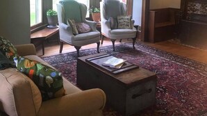 Een gezellige woonkamer met een groot raam, twee fauteuils, een salontafel en een open haard.