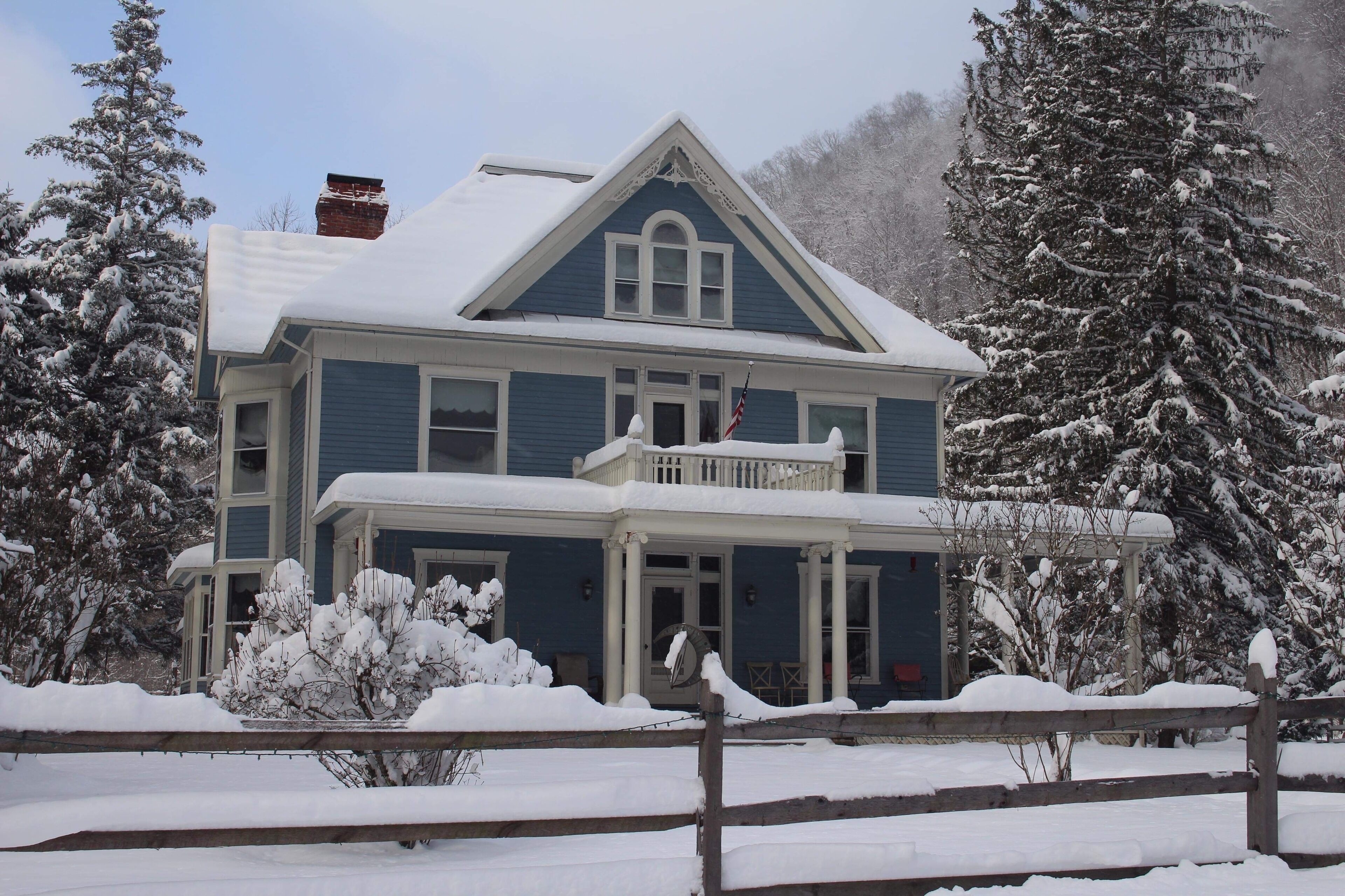 Uma casa de dois andares com telhado coberto de neve e varanda.