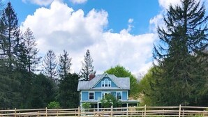 Een huis met een blauw dak en witte details, omringd door een houten omheining en een veld met groene gewassen.