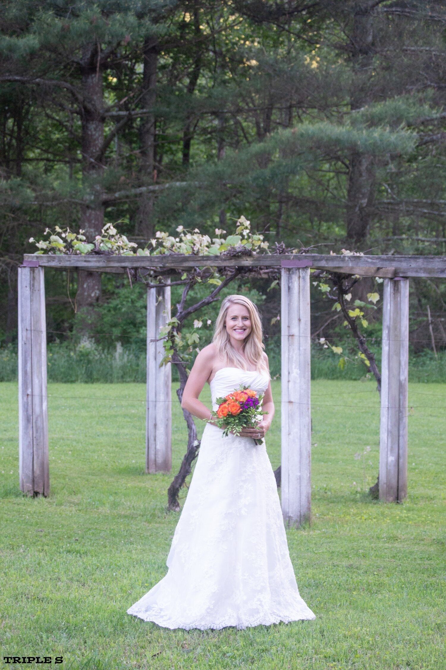 Une cérémonie de mariage se déroulant dans un cadre naturel, avec une arche en bois et de la verdure en arrière-plan.