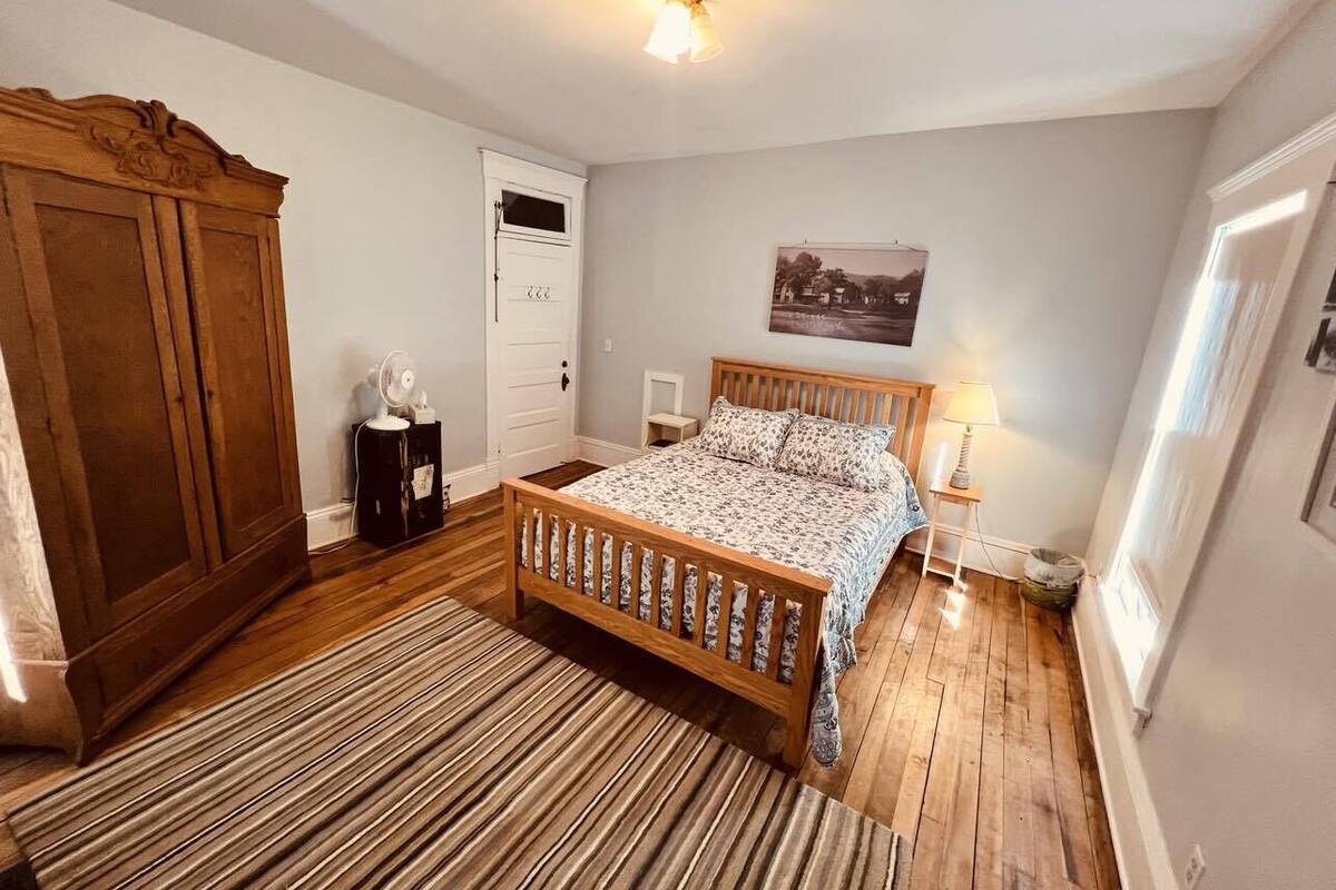 A bedroom with a wooden bed, a wooden wardrobe, a bedside table with a lamp, and a framed picture on the wall.