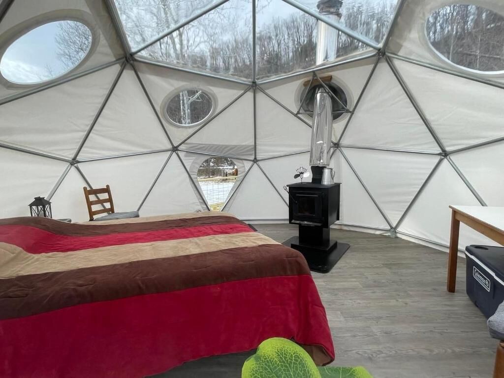 A cozy, circular tent-style room with a bed, a table, and a wood-burning stove.