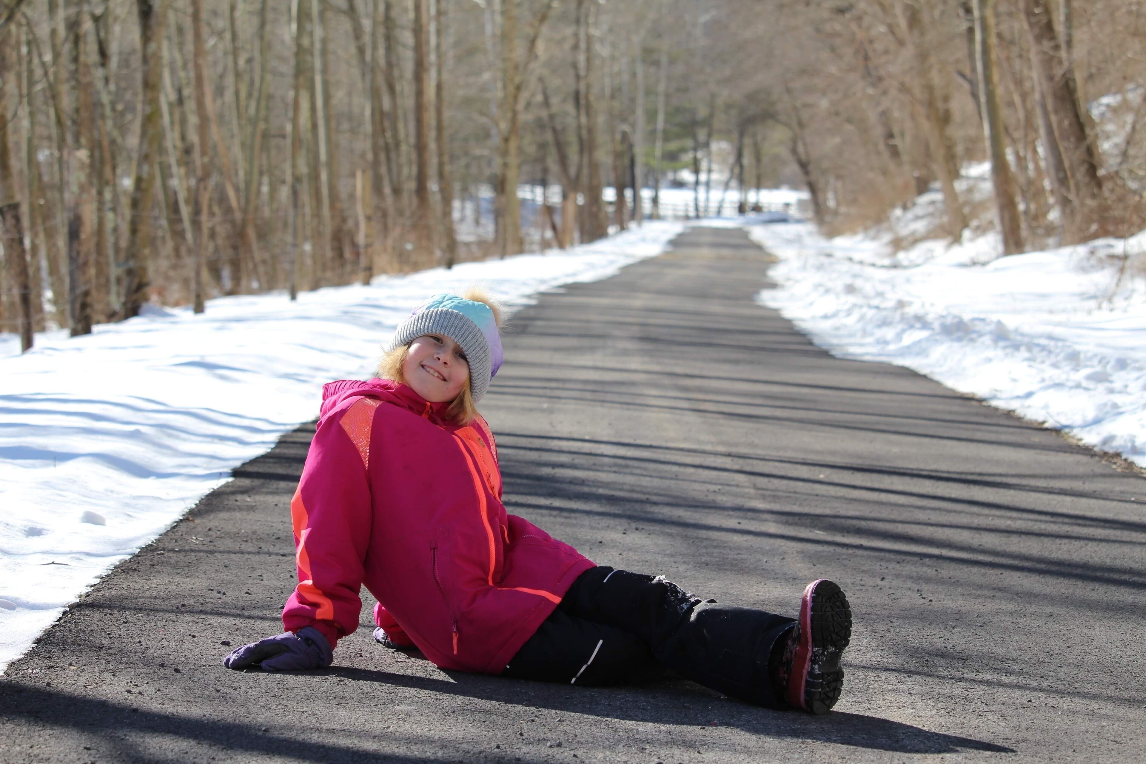 A person sitting on a paved path surrounded by trees.