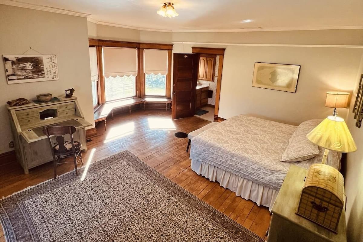 A bedroom with a bed, a desk, a chair, a lamp, and a view of the outside.