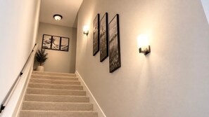 Una escalera con barandilla, escalones alfombrados e iluminación empotrada en la pared.