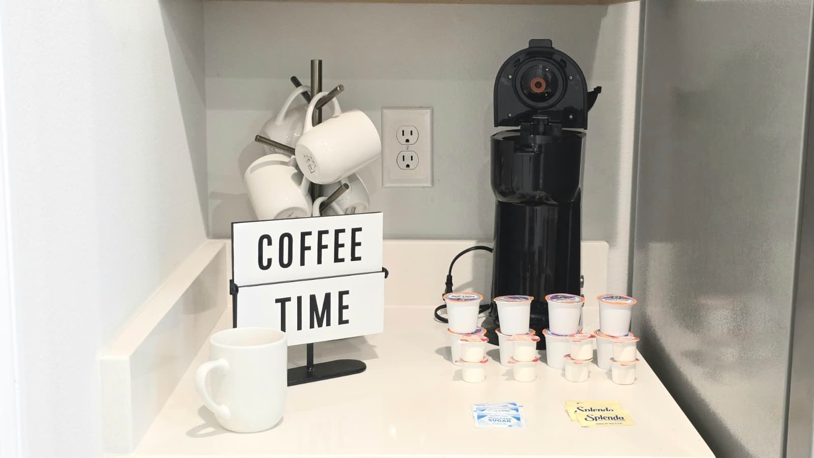 A coffee station with a sign reading 'COFFEE TIME,' a coffee maker, disposable cups, and a sugar packet.