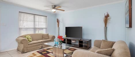 A living room with two sofas, a coffee table, a flat-screen TV, and a ceiling fan.