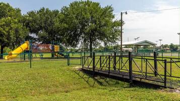 A playground with a yellow slide and a fenced area, surrounded by trees and a covered pavilion.