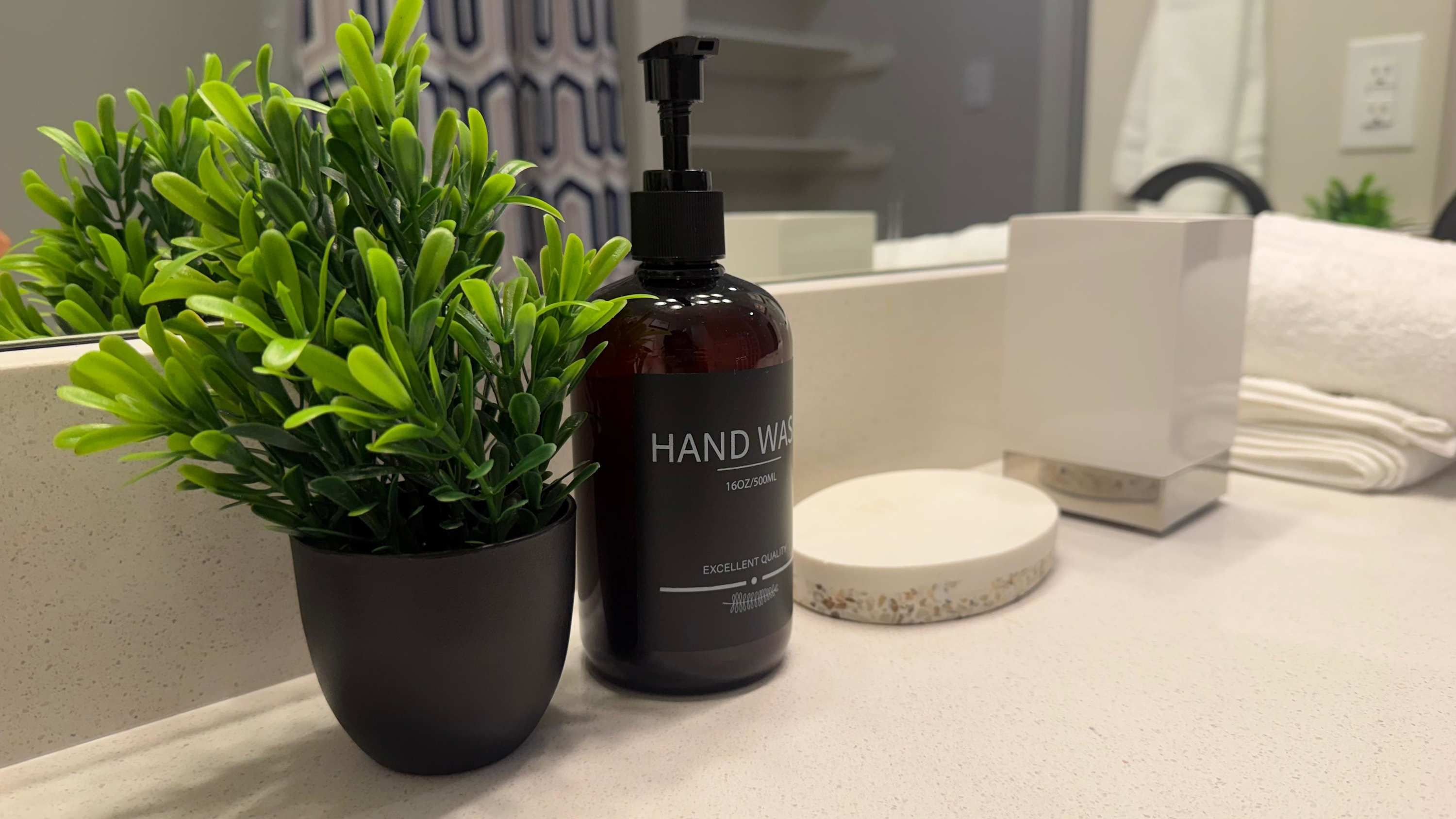 Een badkamermeubel met een handzeepdispenser, een potplant en een stapel handdoeken.