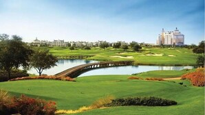 A golf course with a bridge over a pond, surrounded by greenery and a large hotel in the background. - 3 bedroom townhouse in a Golf community near Disney parks. (Kissimmee)