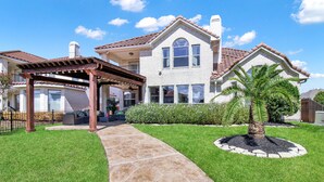 A two-story house with a covered patio, a stone pathway, and a well-maintained lawn. -  truly stunning lakefront with immediate access to all the city has to offer. (Cypress)