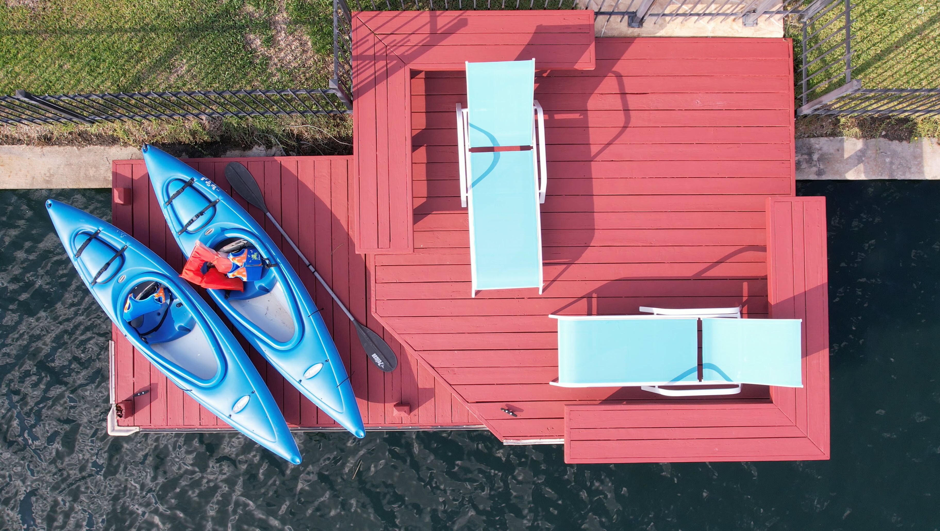 A red dock with two kayaks and a paddleboard, a lounge chair, and a table.