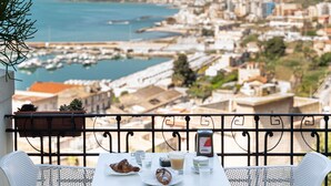Un balcon avec une table préparée pour le petit-déjeuner, offrant une vue sur un port de plaisance et le paysage urbain.