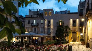 A courtyard with outdoor seating, a flower garden, and buildings with balconies and lights.